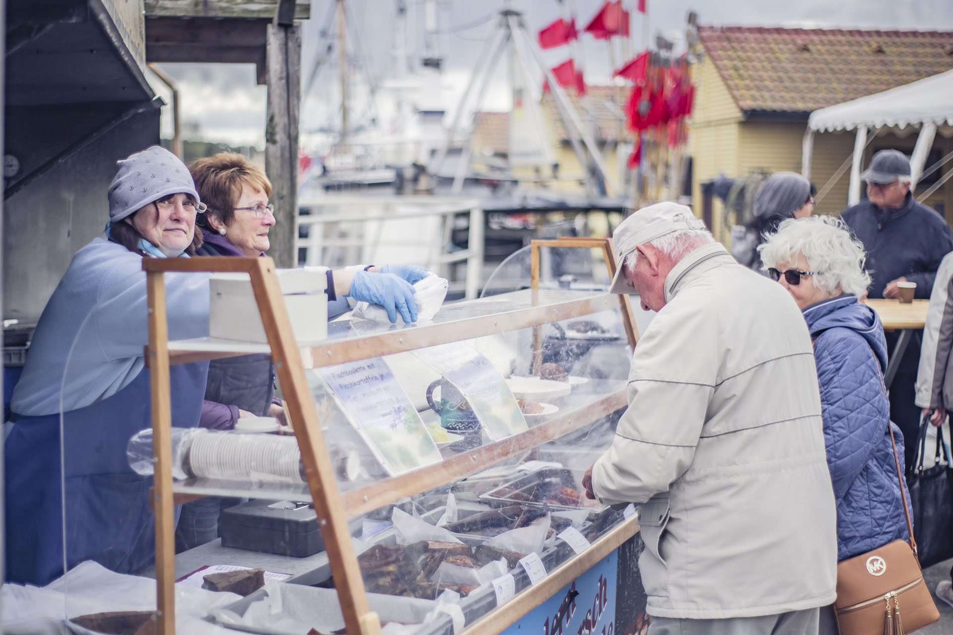 Ein älteres Paar an einem Fischstand, hinter dem zwei Dame stehen.